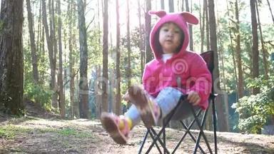 亚洲小女孩坐在椅子上，和家人<strong>一起去</strong>松林露营。 户外活动的概念